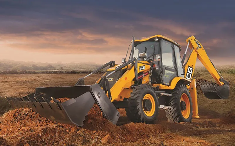 Backhoe loader moving soil at sunset